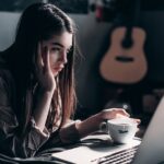 photo of woman lying on bed while using laptop