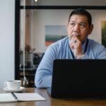 thoughtful ethnic businessman using laptop while working in office