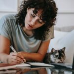 focused young female student doing homework using netbook sitting near cute cat